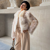 A woman wearing a fur coat and holding a purse stands in front of a stone wall.