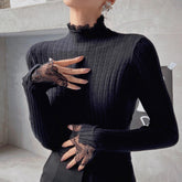 A person wearing a black turtleneck sweater with lace detailing on the sleeves and gloves, posing with their hands on their chest.