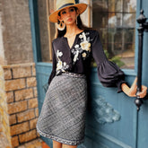 Woman in a stylish outfit with floral top and plaid skirt standing next to a blue door.
