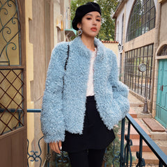 A woman wearing a light blue fuzzy coat, black skirt, and a black hat stands on a balcony with a wrought iron railing.