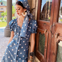 Woman in a blue polka dot dress standing next to a wooden door.