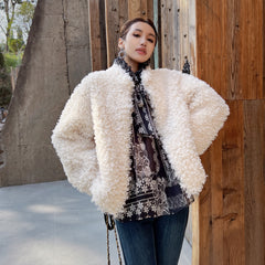 A woman wearing a white fluffy coat and a patterned shirt stands in front of a wooden wall.