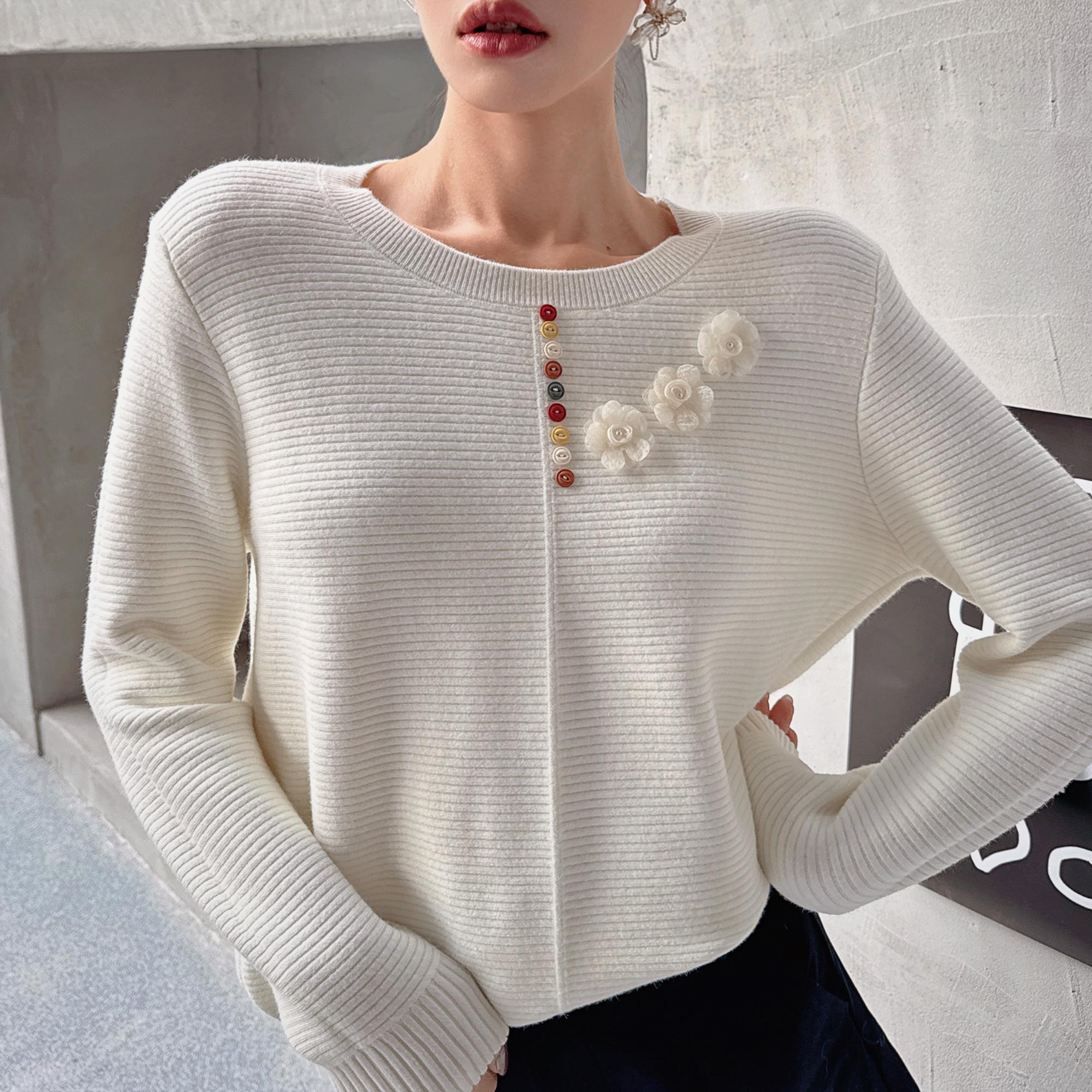A woman wearing a white sweater with colorful flower-shaped buttons on the front.