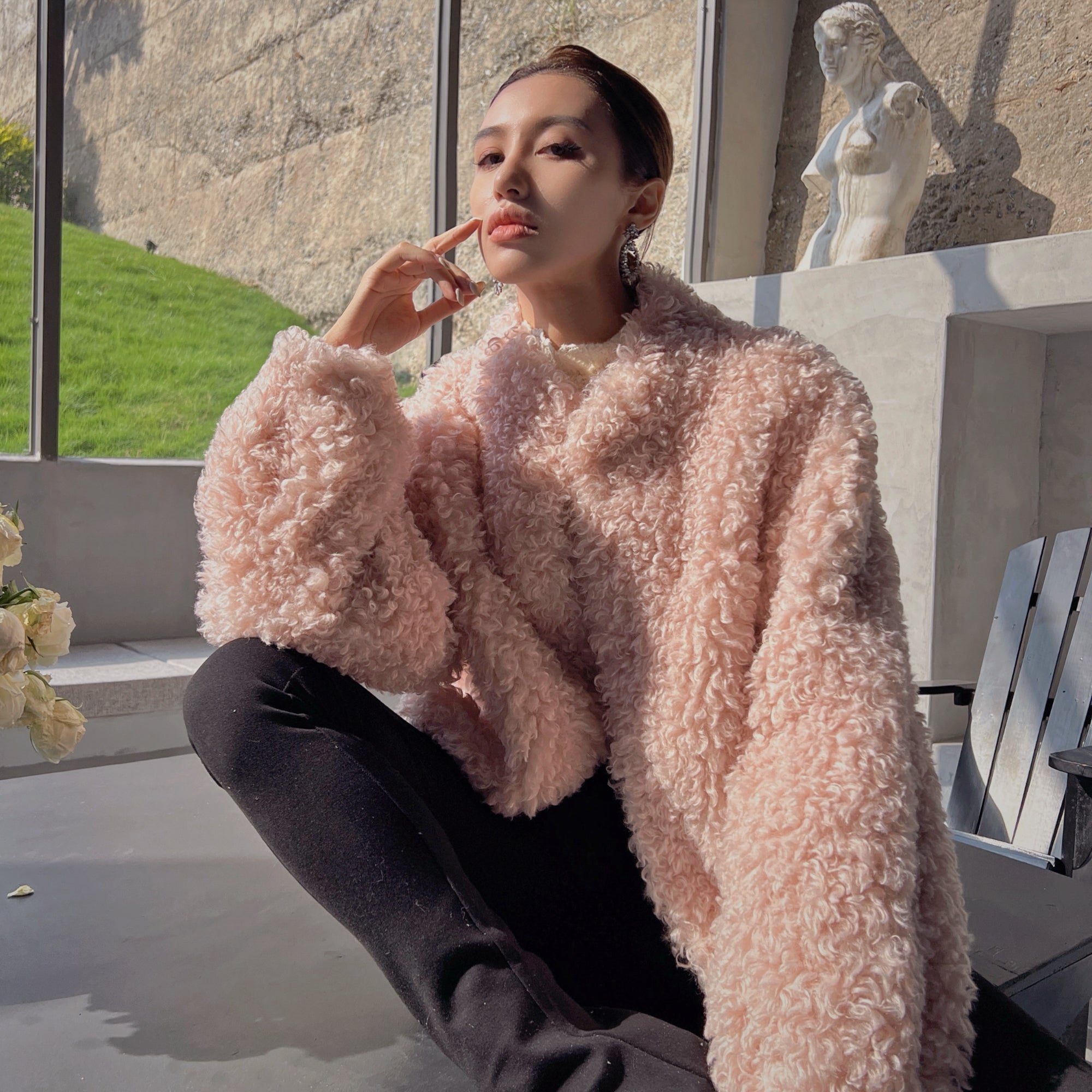 A woman wearing a pink fuzzy coat is sitting on a bench, looking pensive.