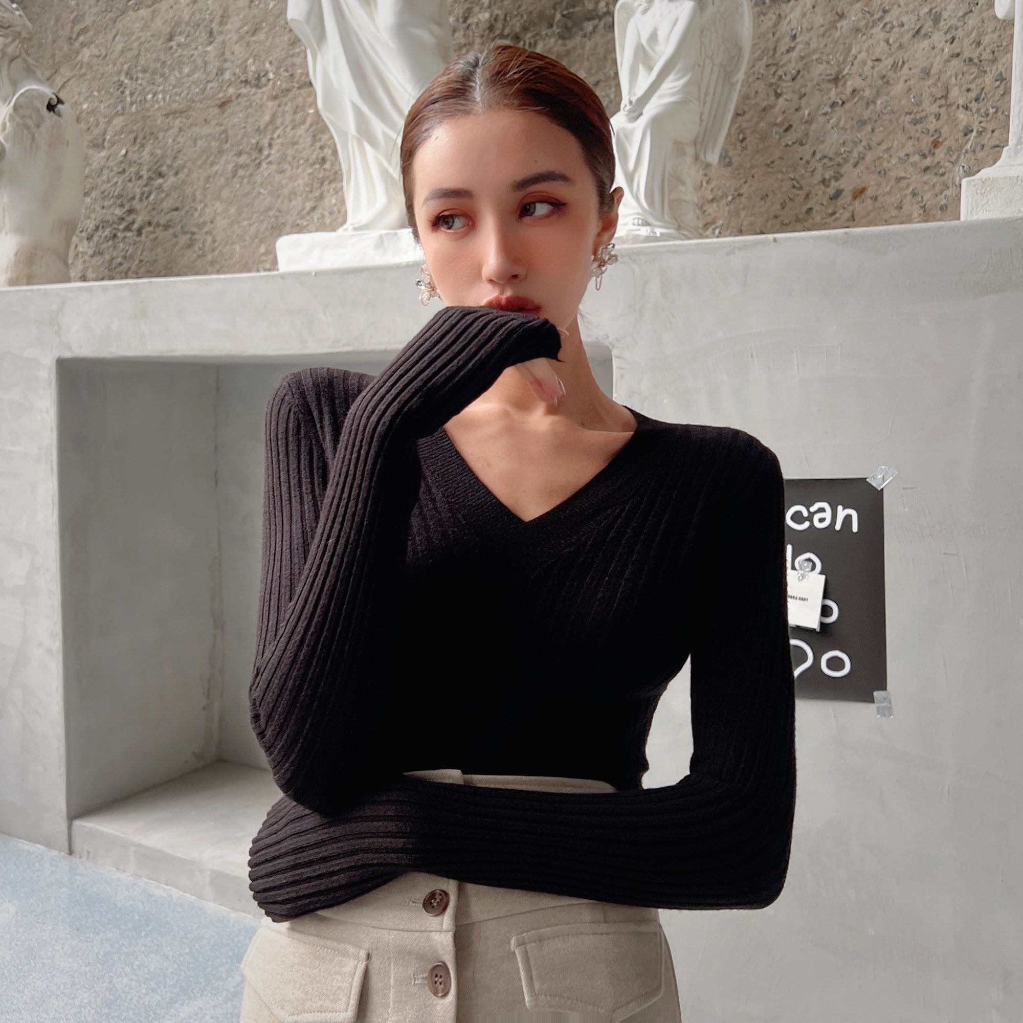 A woman wearing a black sweater stands in front of a concrete wall, with a sign that says "can do anything".