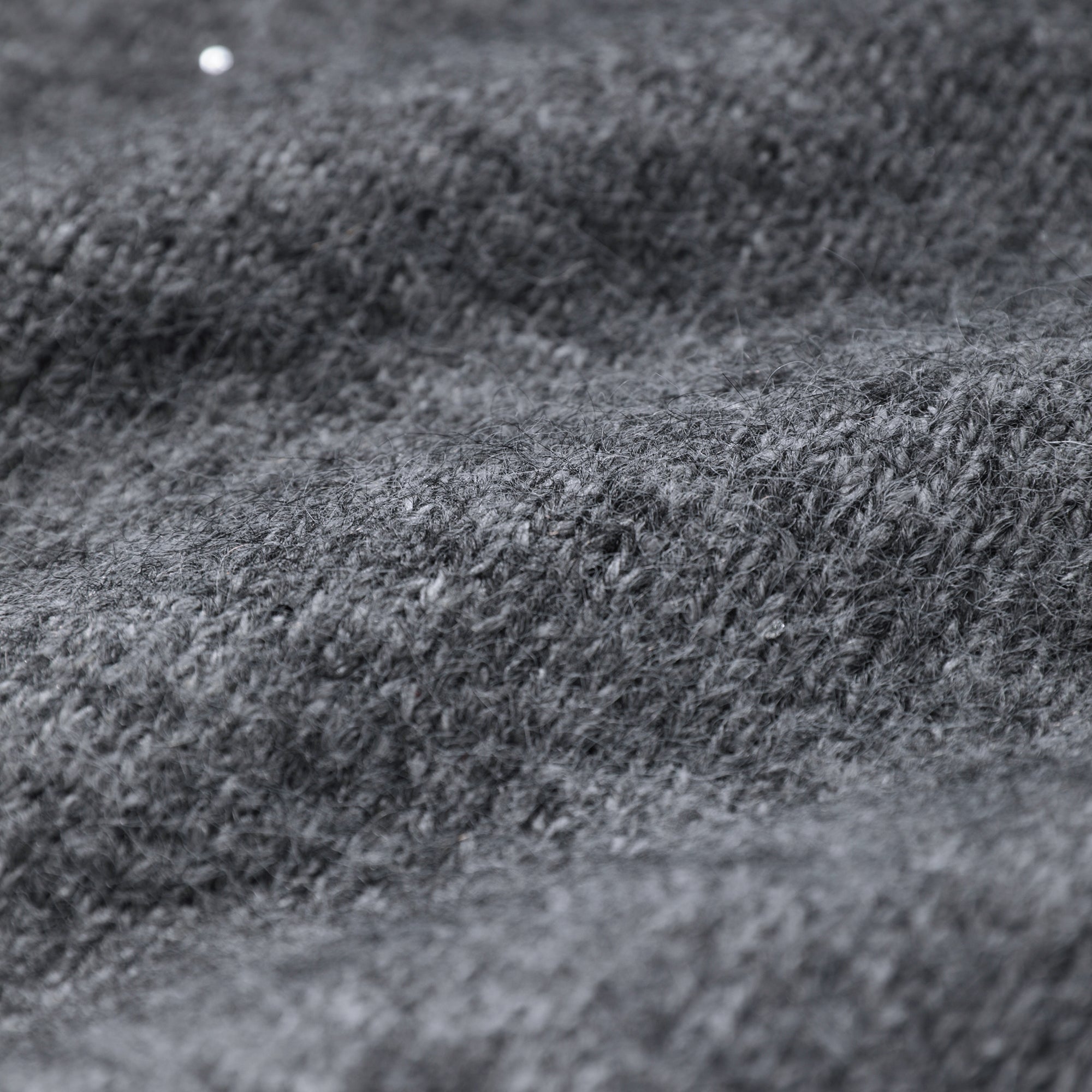 A close-up view of a textured gray fabric, possibly a sweater or blanket, with a small white dot in the top left corner.