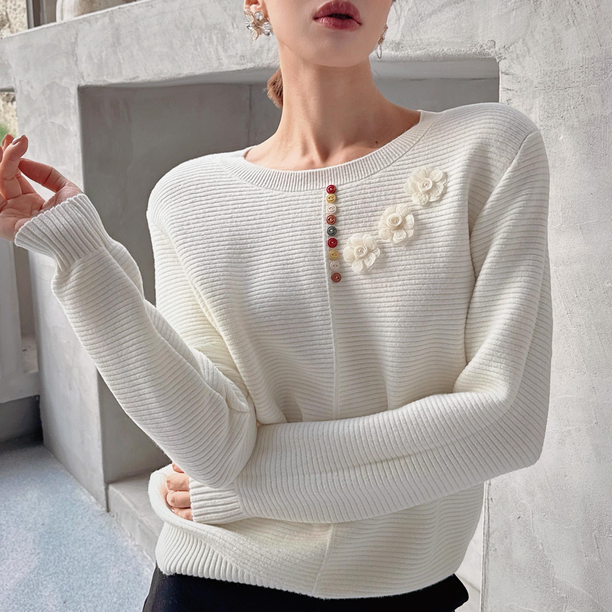A woman wearing a white sweater with a floral design and colorful buttons on the front.