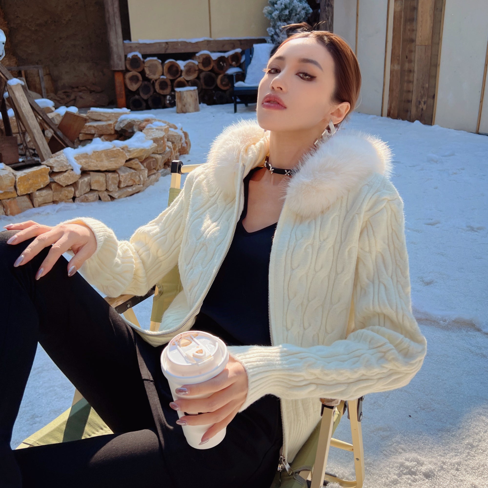 A woman in a white sweater sits in a chair, holding a coffee cup, with a snowy outdoor scene in the background.