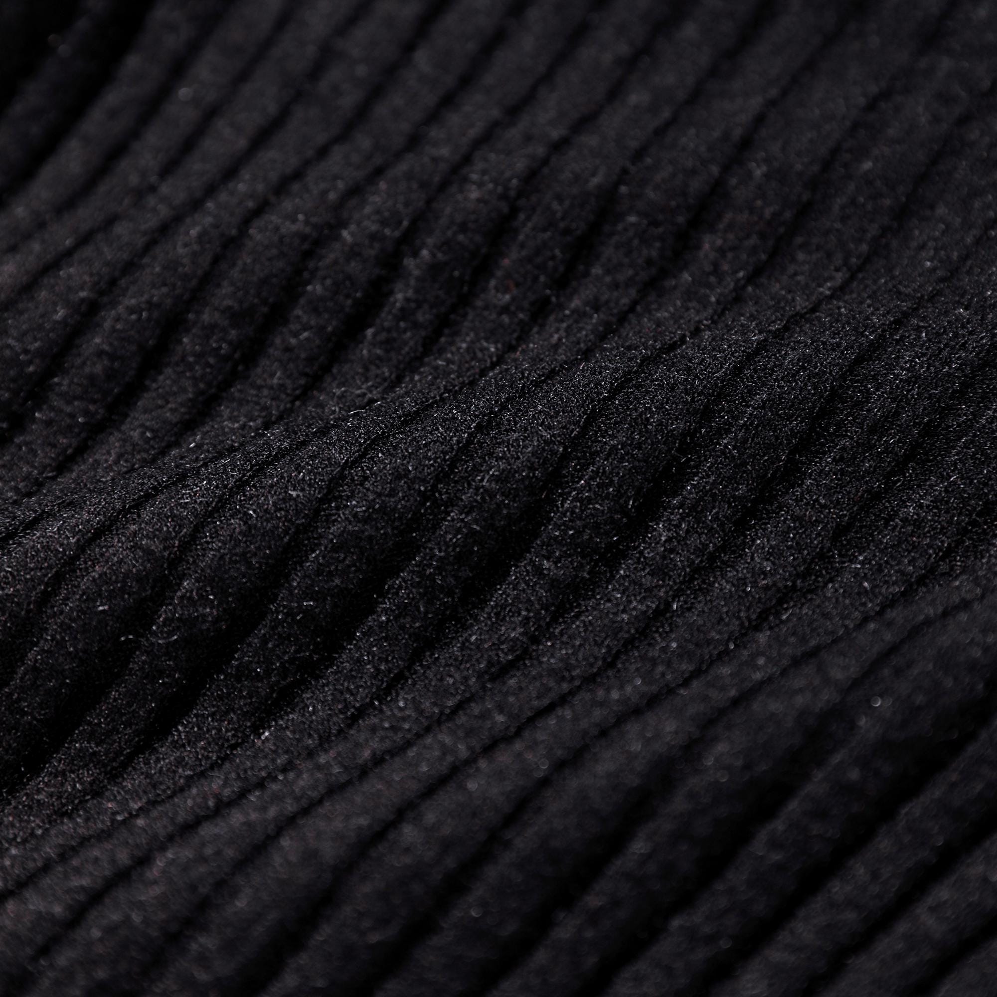 The image is a close-up of a dark, textured fabric with a ribbed or crisscross pattern, creating a sense of depth and texture.