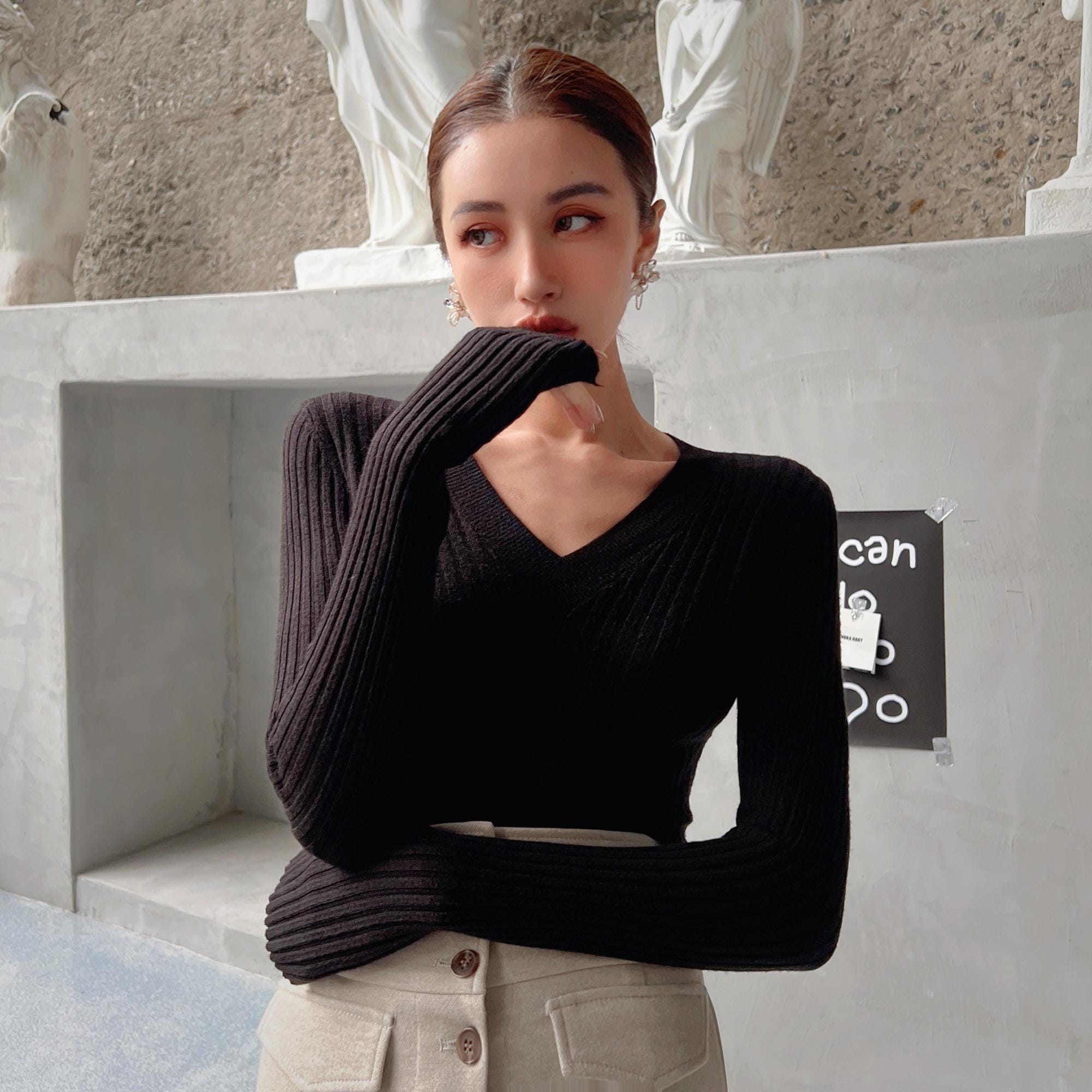 A woman wearing a black sweater stands in front of a concrete wall, with a sign that says "can do anything".