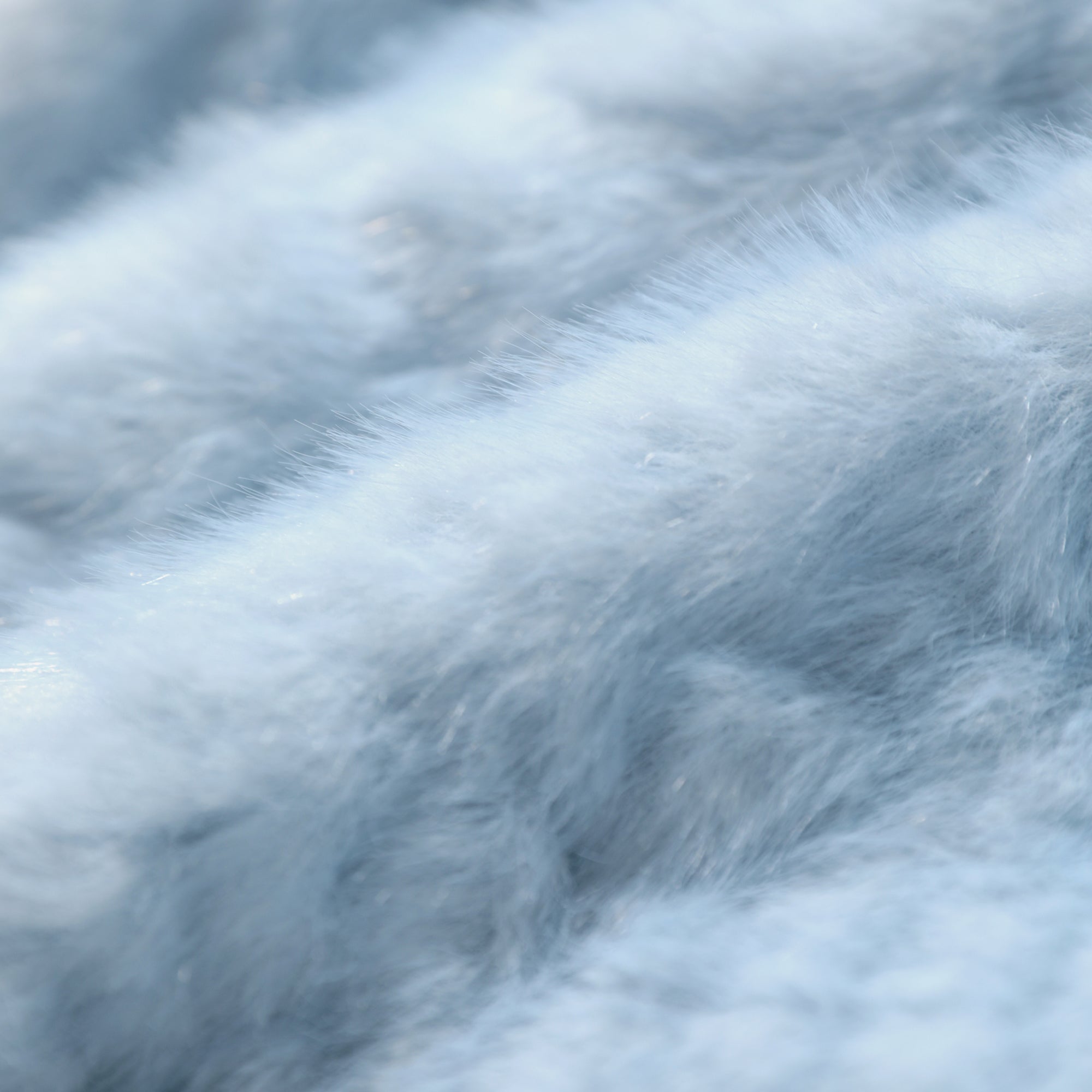 A close-up view of a soft, fluffy white fur texture, with a blurred background that emphasizes the texture and softness of the material.