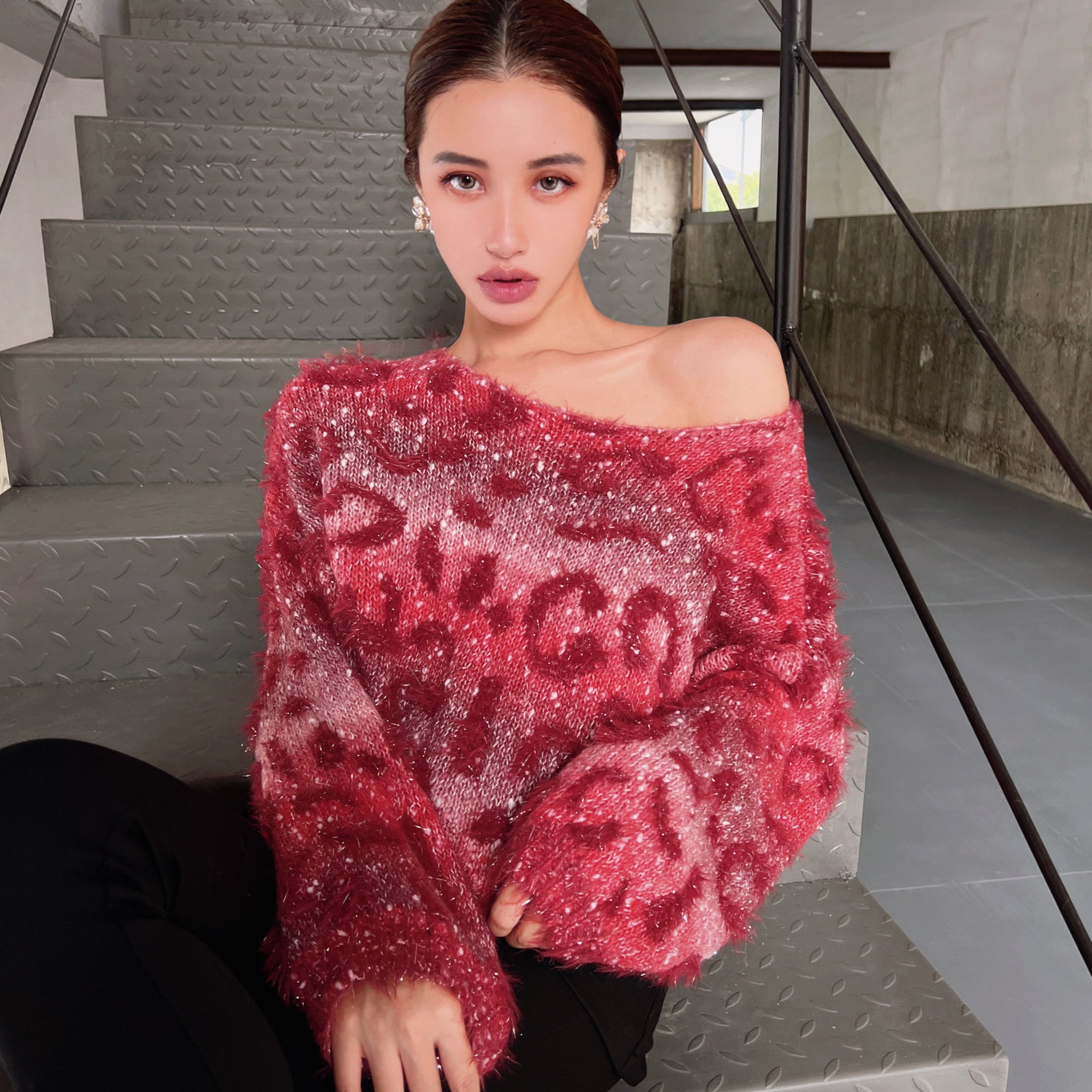 A woman wearing a red patterned sweater is sitting on a staircase.