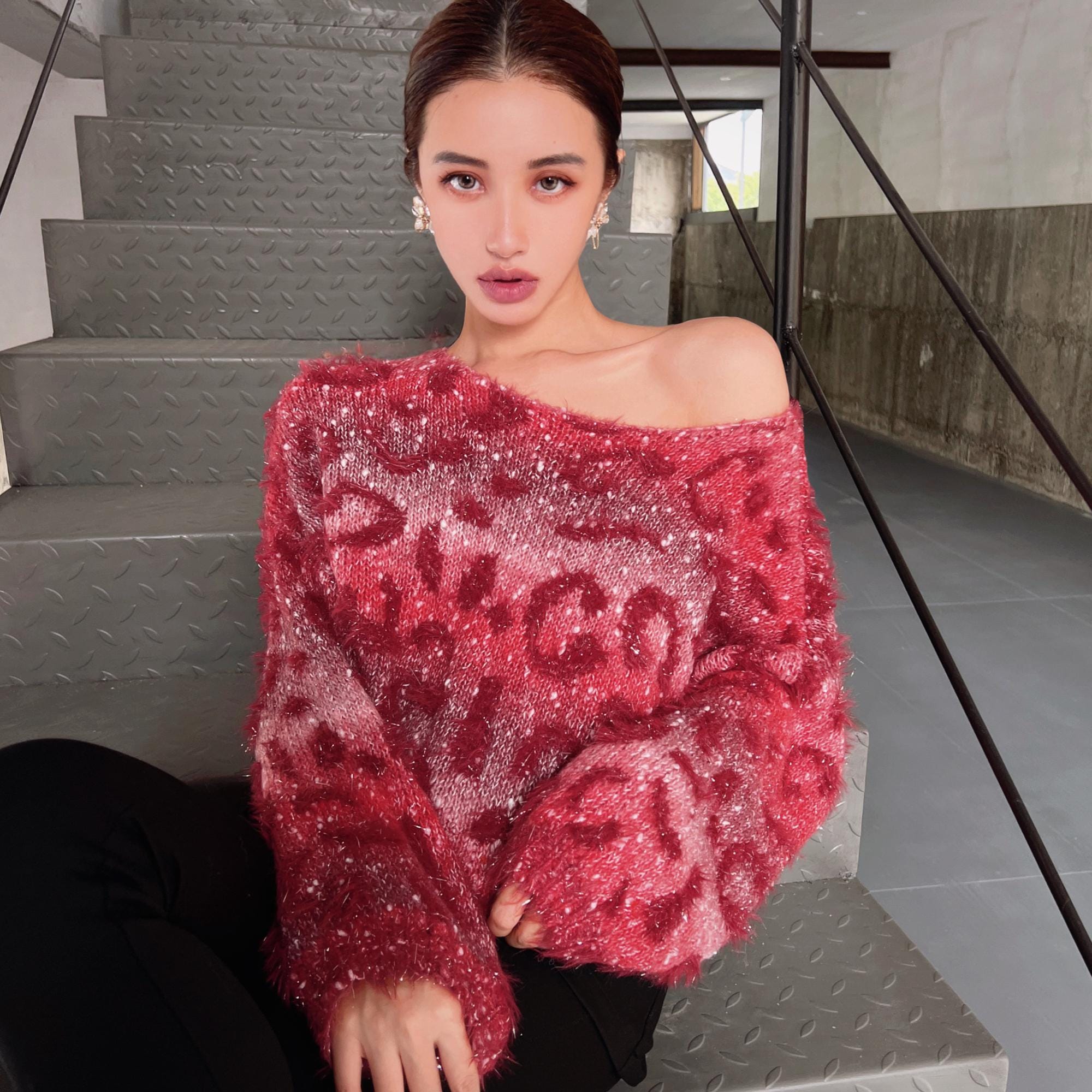 A woman wearing a red patterned sweater is sitting on a staircase.