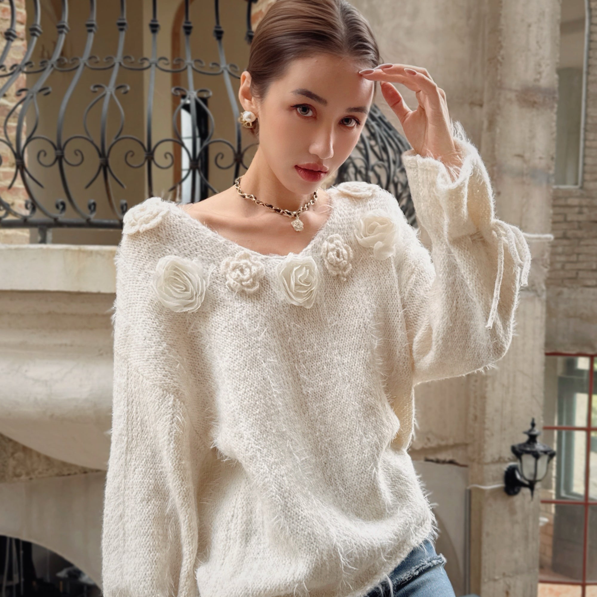 A young woman wearing a white sweater with flower designs poses for a portrait.