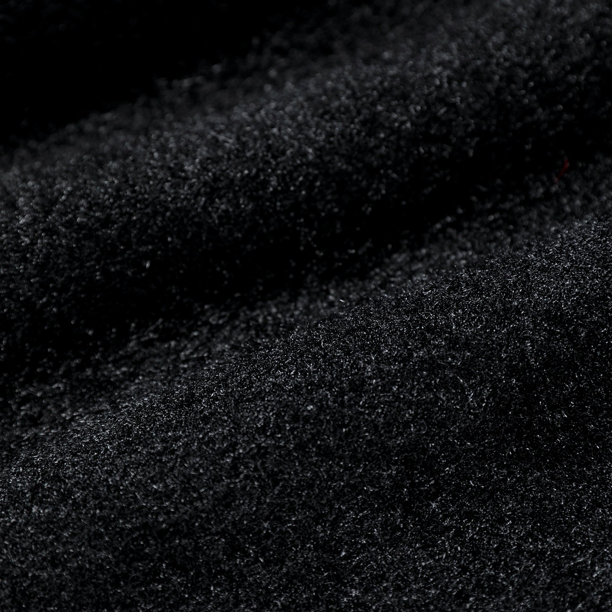 The image is a close-up of a black, textured surface, possibly a fabric or a material with a fuzzy texture.
