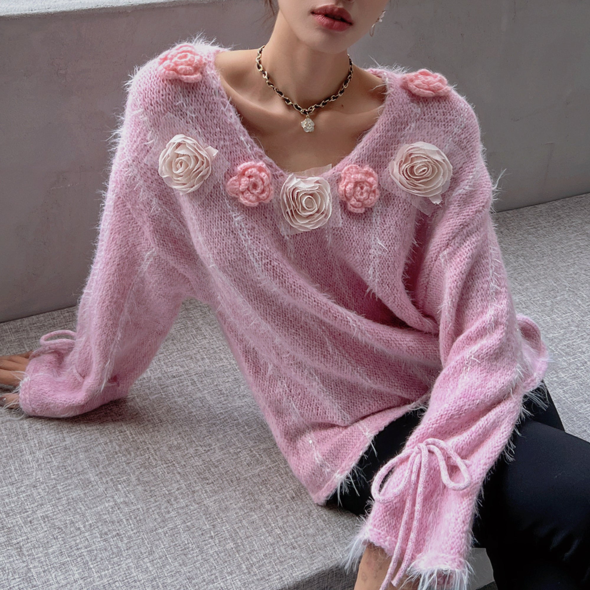 A woman wearing a pink sweater with pink flowers on the front, sitting on a gray surface.