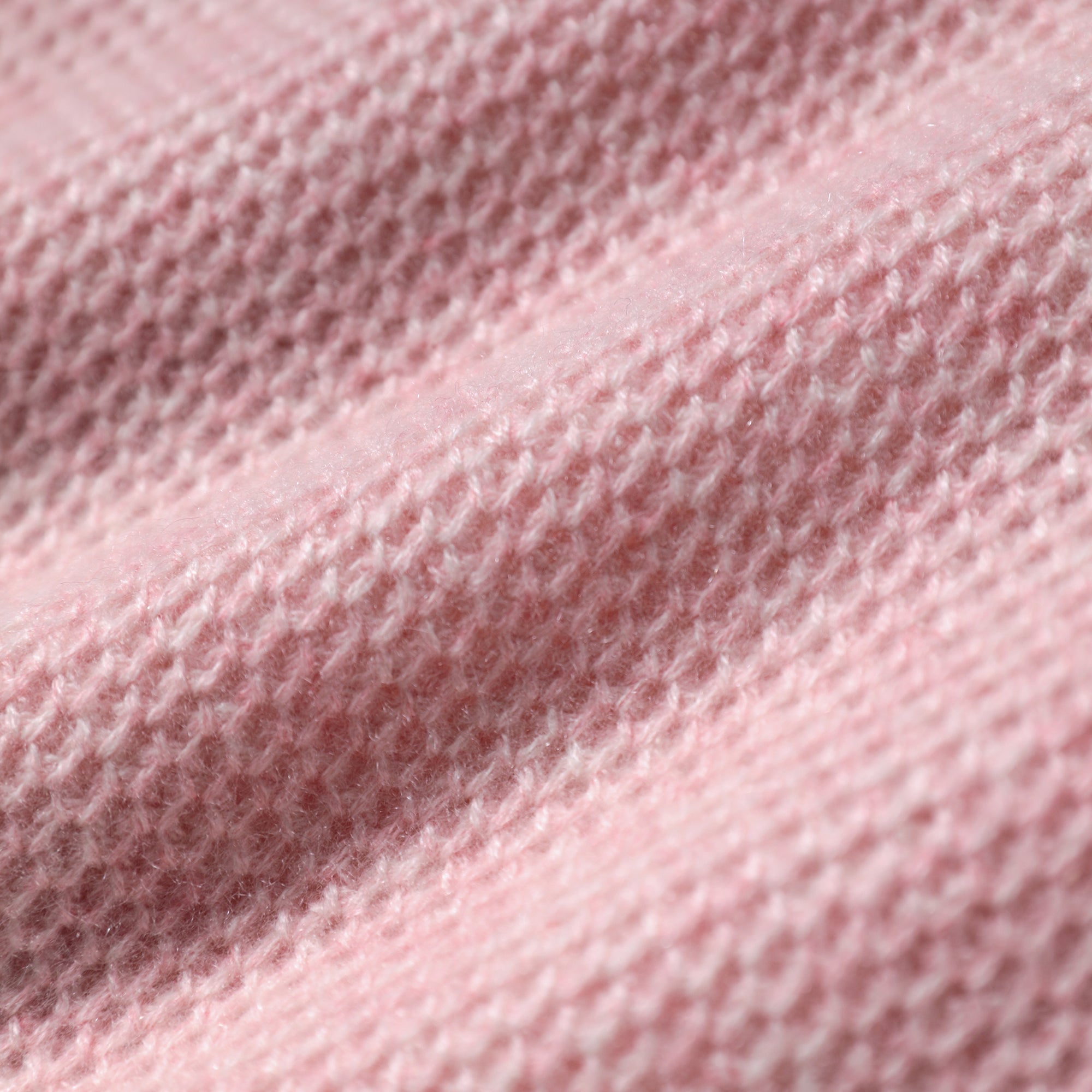 A close-up image of a soft, pink knitted fabric with a textured, woven appearance.