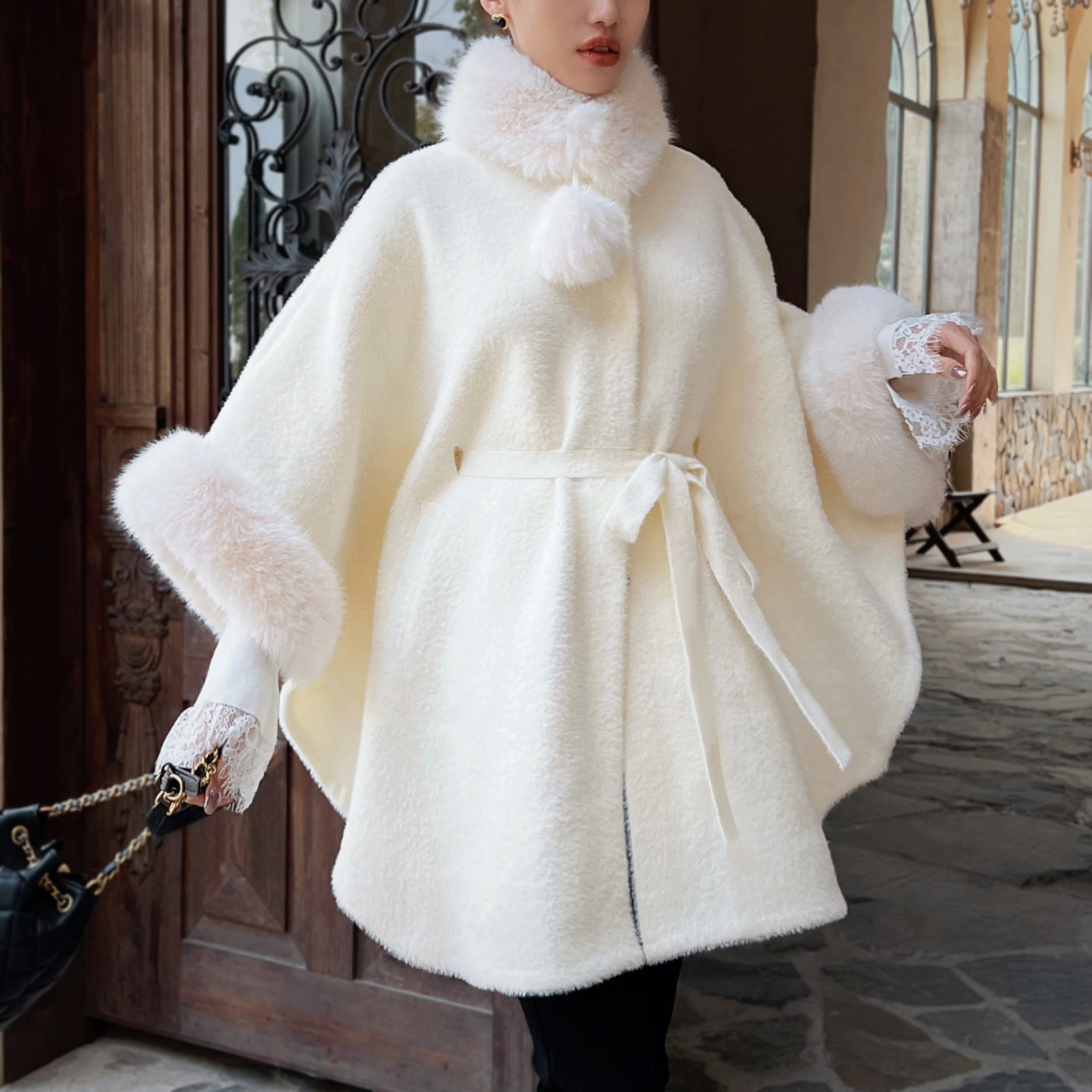 A woman wearing a white fur-trimmed cape-like garment with a white lace trim, standing in front of a wooden door.