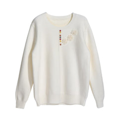 A white knitted sweater with a floral design on the front.