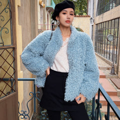 A woman wearing a light blue fuzzy coat, black skirt, and a black hat stands on a balcony, with a building and a clock visible in the background.