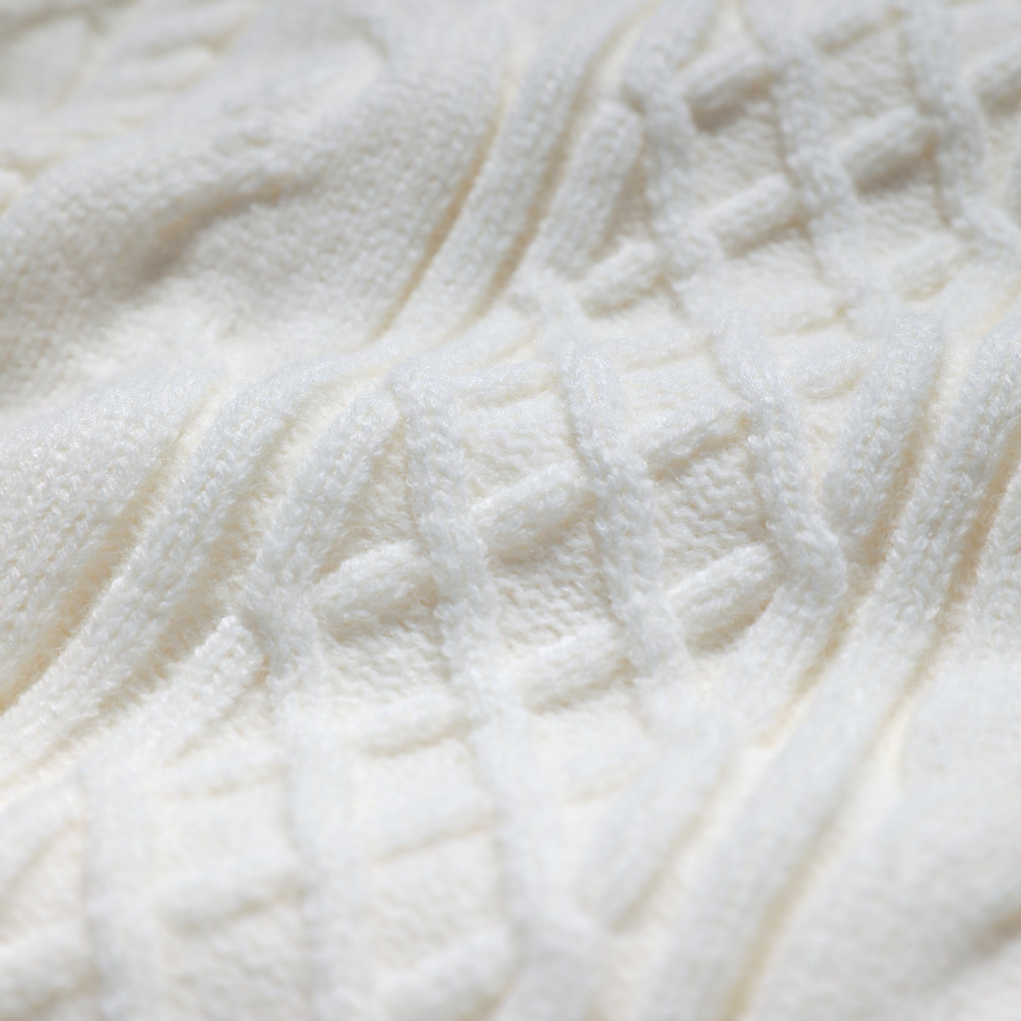 A close-up image of a white knitted fabric with a criss-cross pattern.