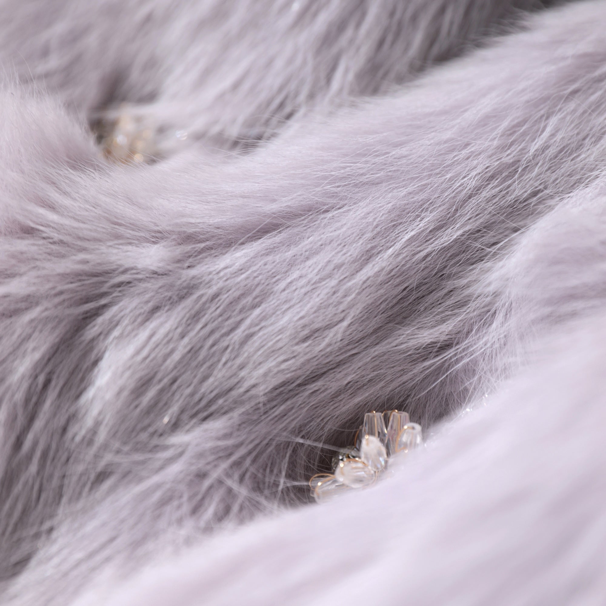 A close-up image of a soft, fluffy gray fur texture with small, clear, and shiny embellishments, such as crystals or pearls, visible in the center.