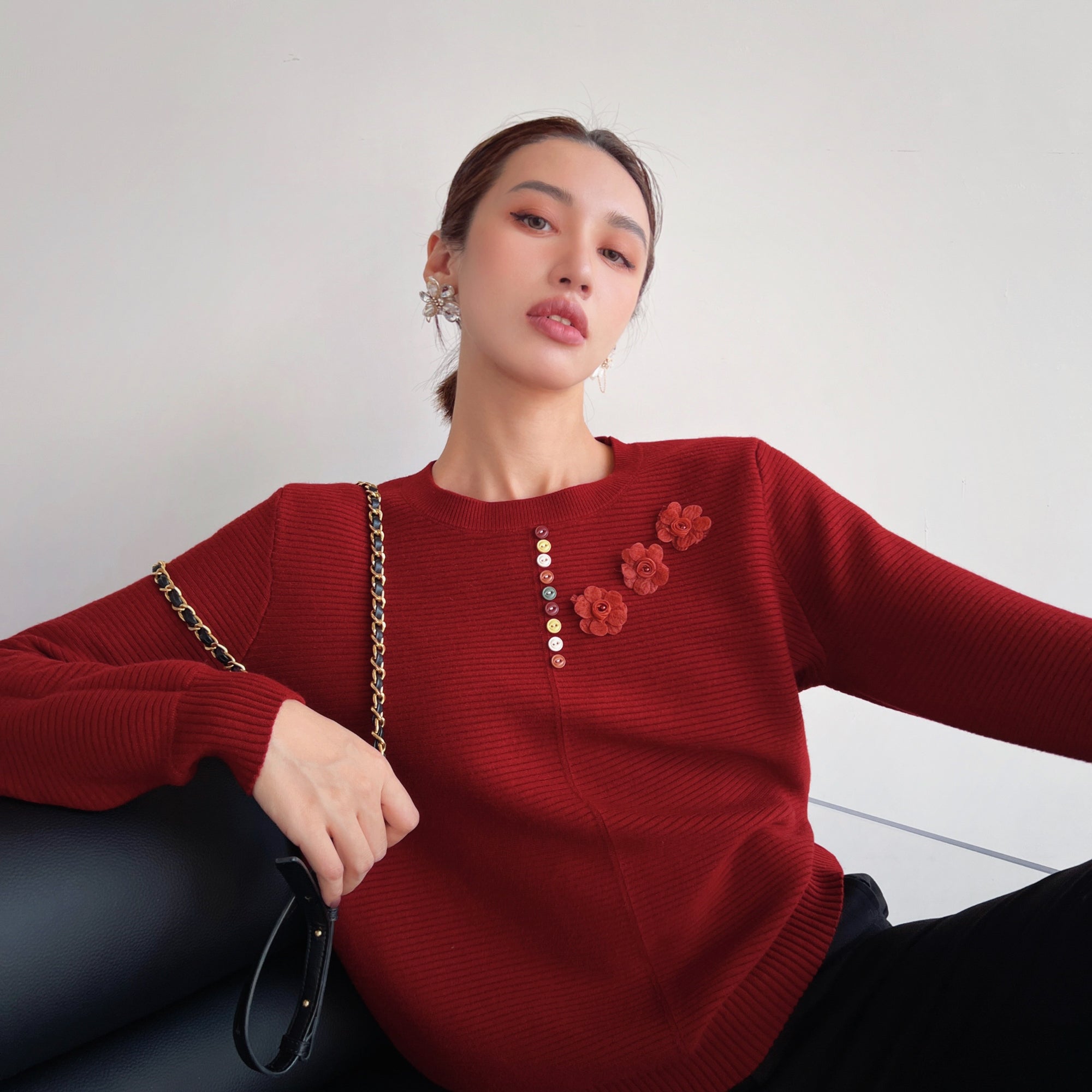 A woman wearing a red sweater with red flowers on it, posing for a photograph.