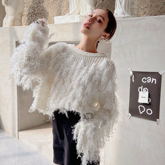A woman wearing a white sweater with fringe poses in front of a wall with a sign that says "I can do anything".