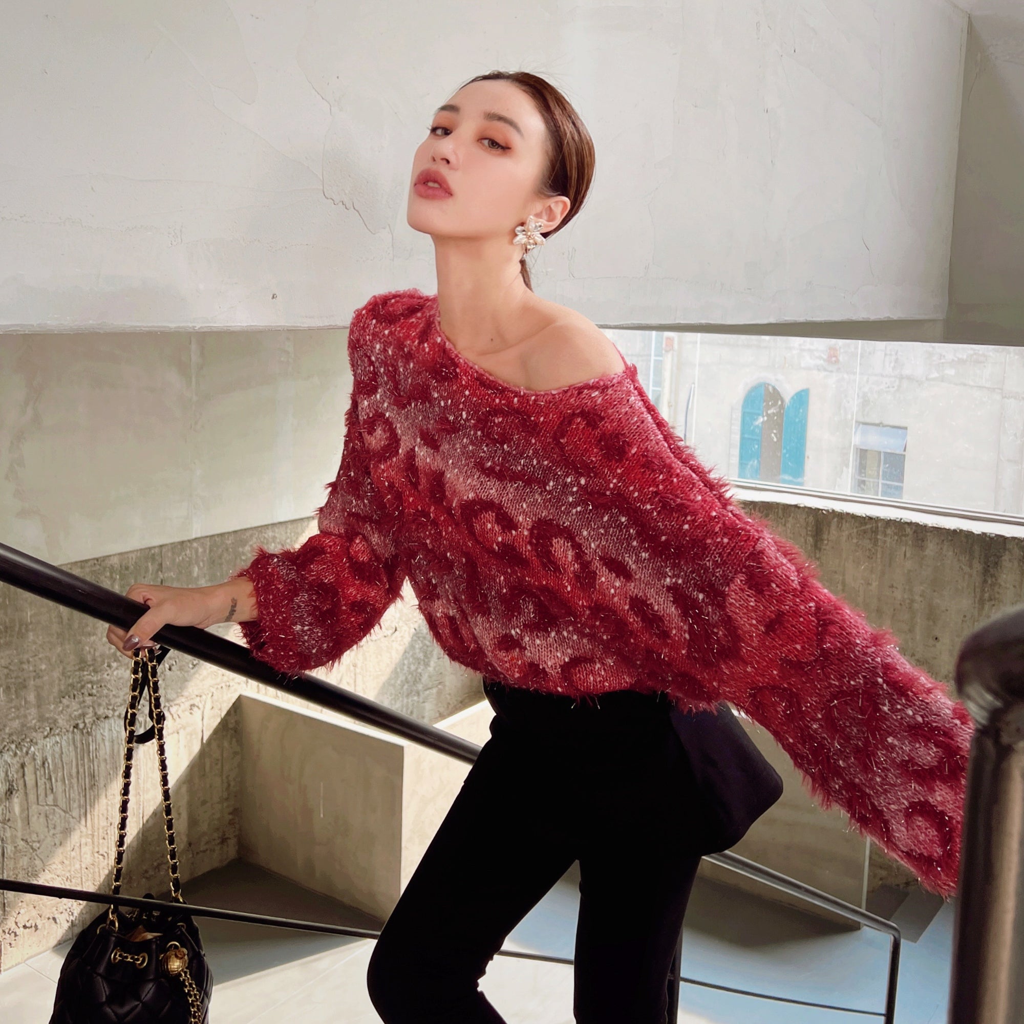 A woman wearing a red patterned sweater and holding a black purse is standing on a staircase.