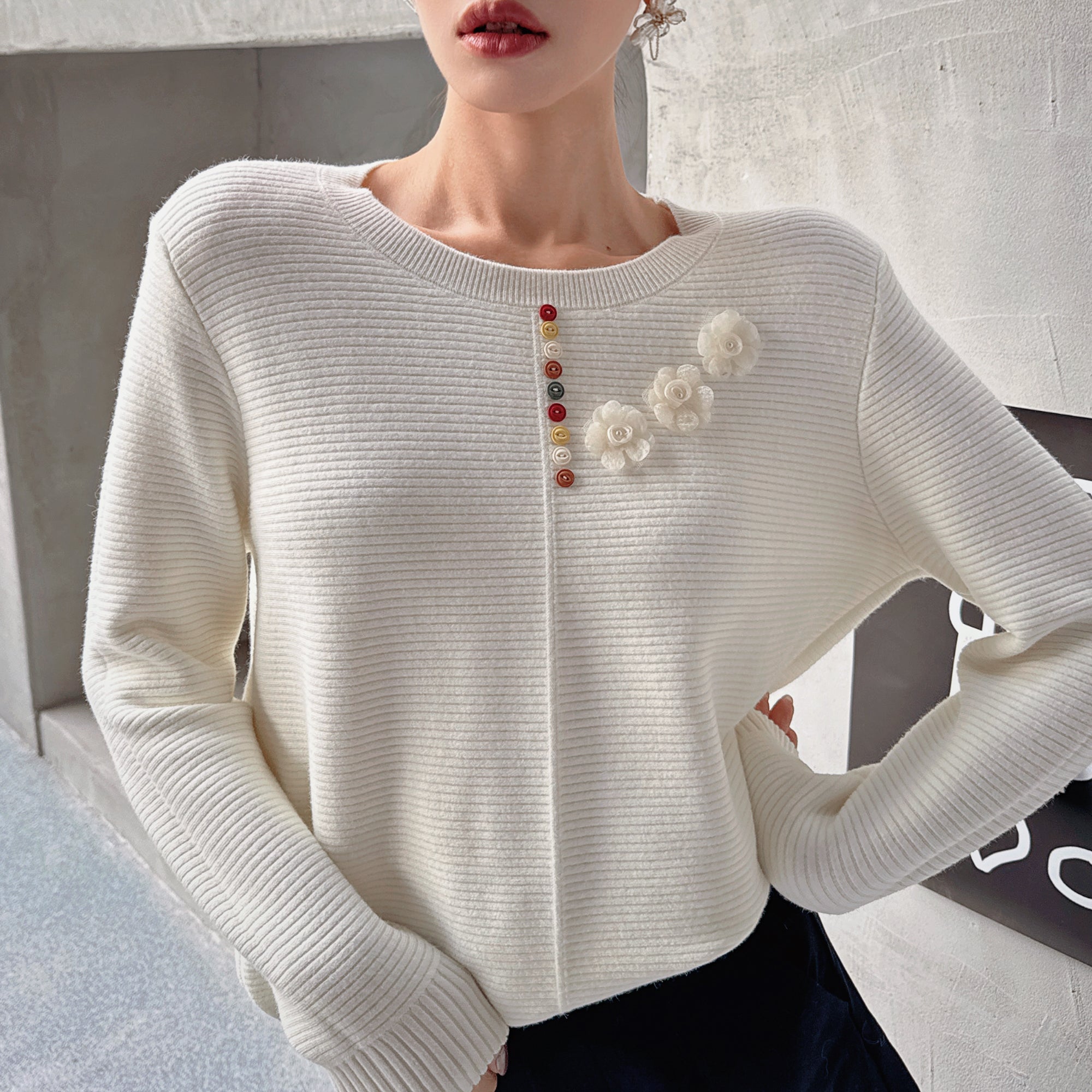 A woman wearing a white sweater with colorful flower-shaped buttons on the front.