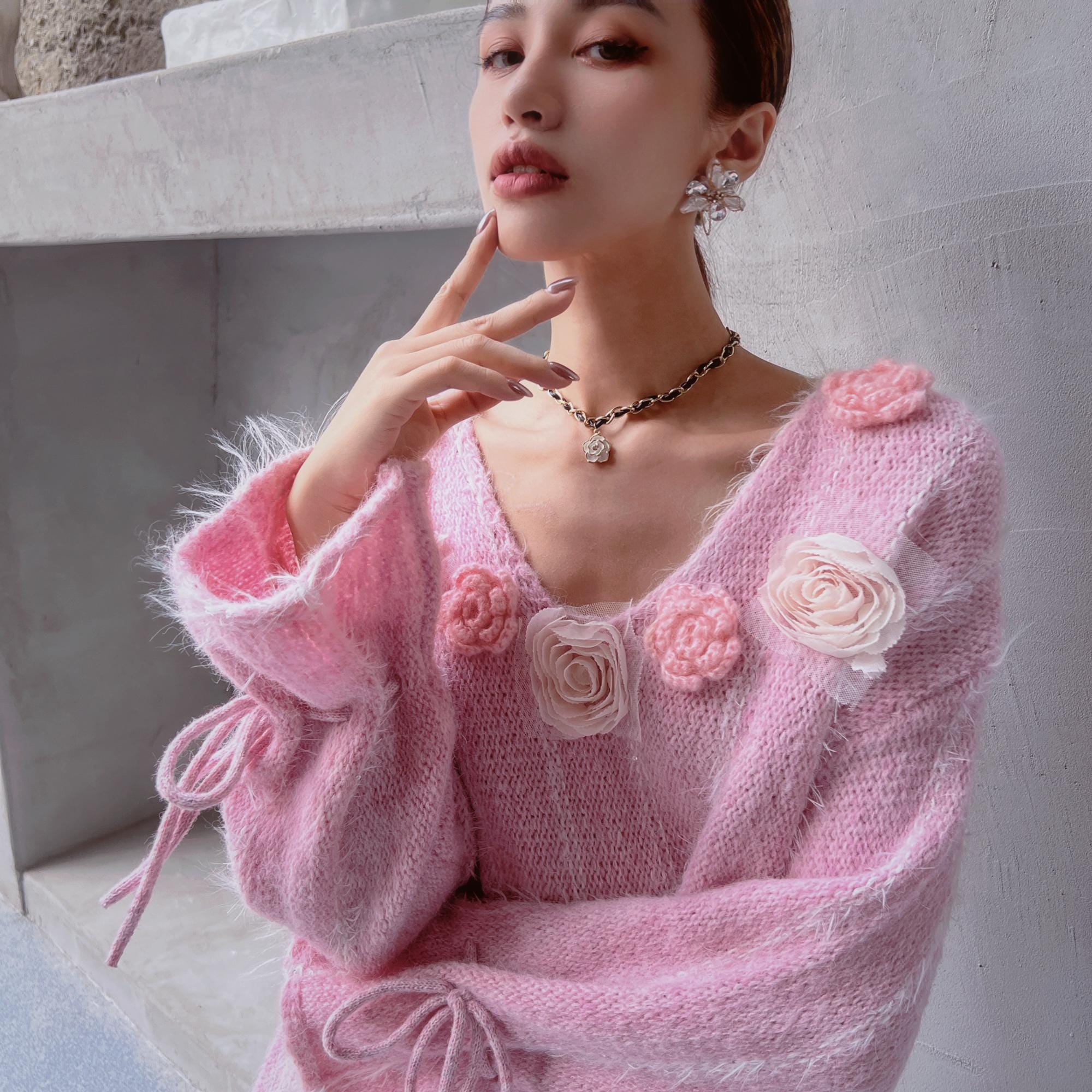 A woman wearing a pink sweater with pink flowers and a necklace is posing for a photograph.
