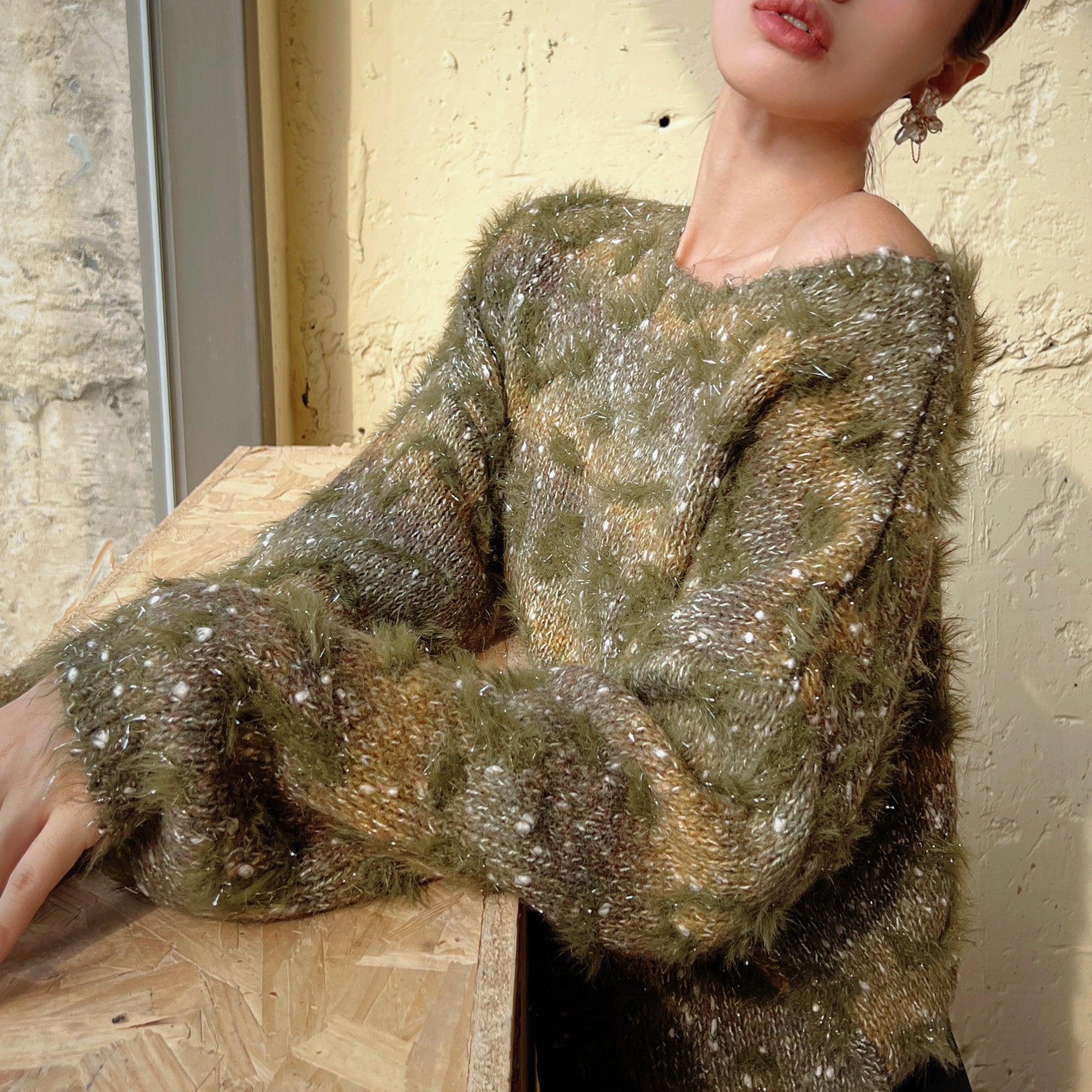 A woman wearing a green and brown fuzzy sweater is leaning against a wooden table.