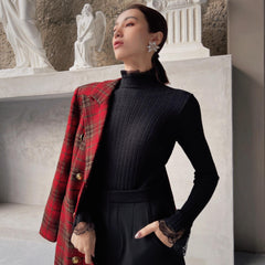 A woman wearing a black sweater and a red plaid jacket stands in front of a stone wall with statues.