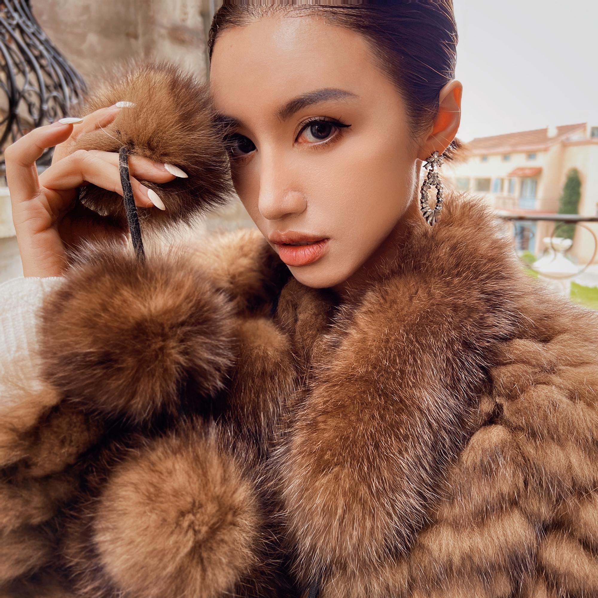 A woman wearing a brown fur coat and earrings is posing for a portrait.