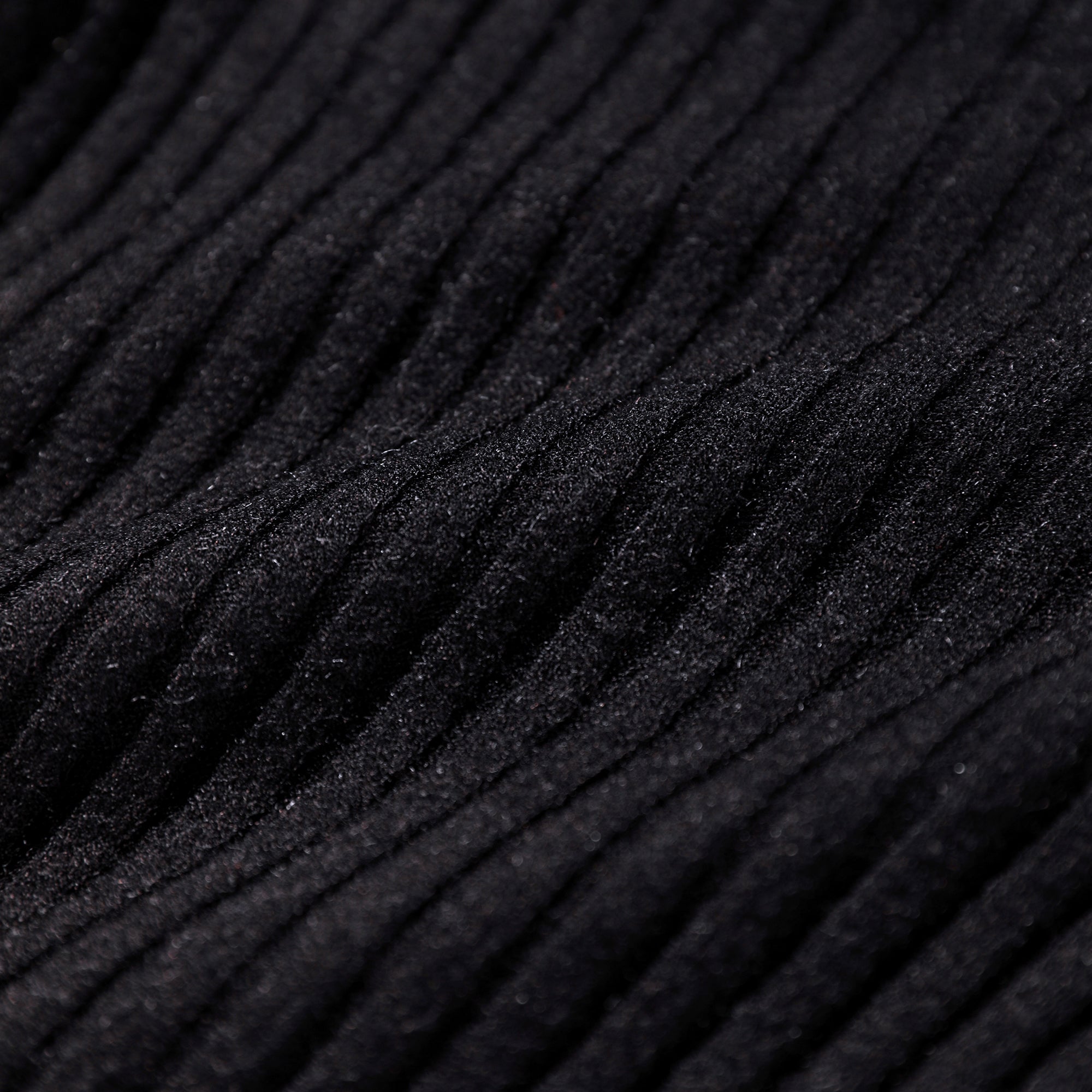 The image is a close-up of a dark, textured fabric with a ribbed or crisscross pattern, creating a sense of depth and texture.