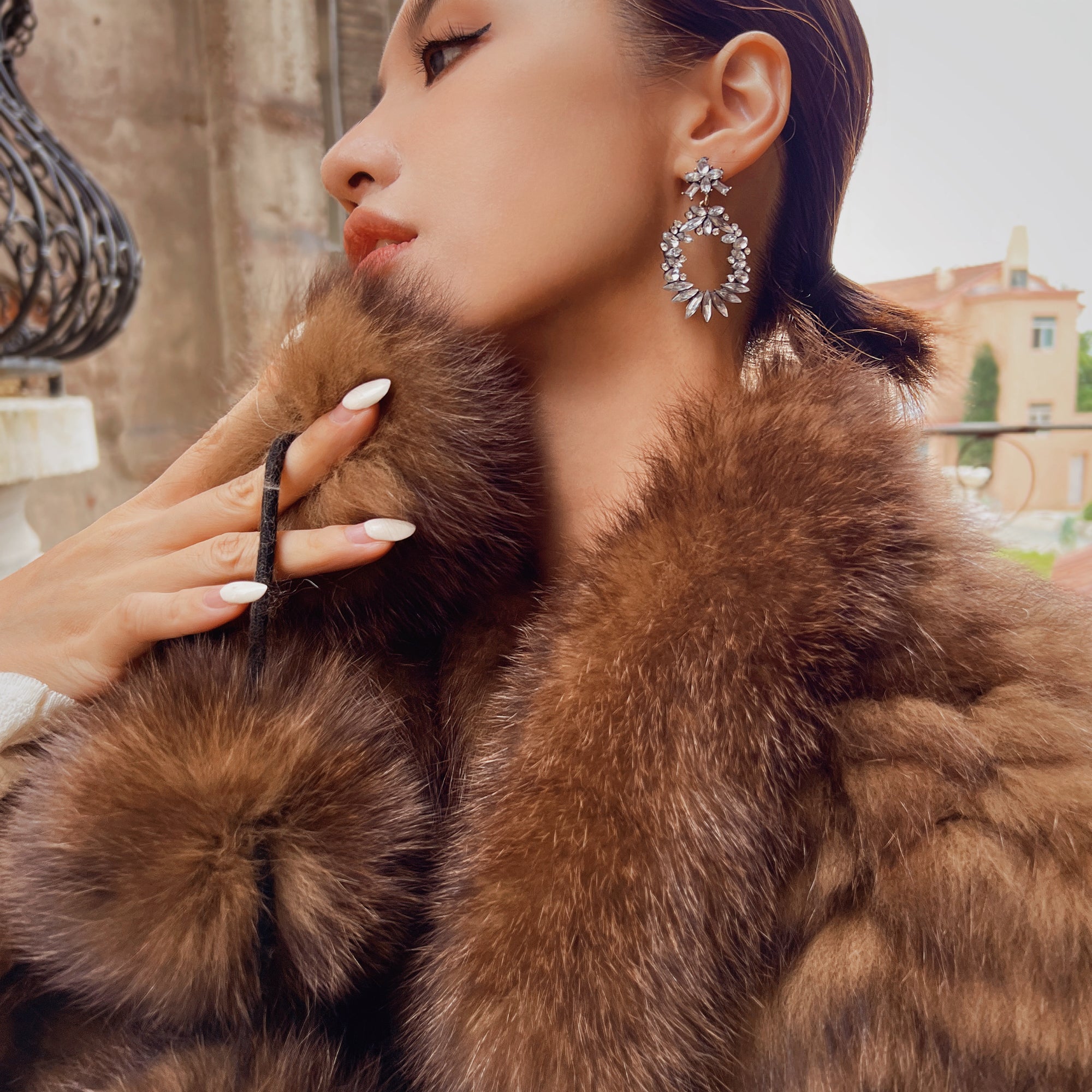 A woman wearing a brown fur coat and large earrings is shown in a close-up portrait.